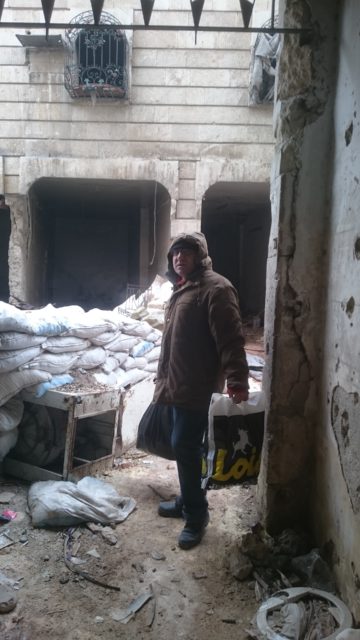 Issa in the entrance of his building. On the back the frontline where the civil war reached Aleppo’s street under Touma’s window.